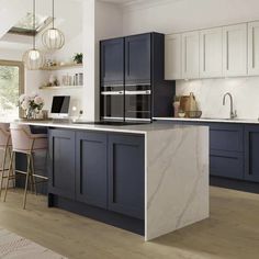 a modern kitchen with blue cabinets and marble counter tops is pictured in this image, there are two bar stools at the center of the island