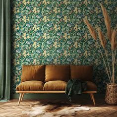 a brown couch sitting in front of a green wall with flowers and leaves on it