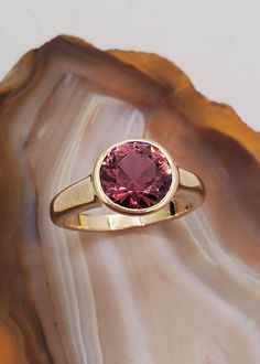 DEN2407 Pink tourmaline solitaire ring. Elegant bezel set ring designed for comfort and style set with Maine Pink Tourmaline.  Ring mounting is low profile 14k yellow gold.  Round brilliant cut pink tourmaline is 2.20cts, approximately 8.5mm in diameter. This stone is from the 1972 Dunton Quarry Newry, ME discovery. Currently the ring is size 5.5 but we will resize at no extra charge if needed. Please specify ring size at checkout. Yellow Gold Solitaire Ring, Yellow Gold Solitaire, Ring Elegant, Pink Tourmaline Ring, Bezel Set Ring, Ring Bezel, Gold Solitaire Ring, Opal Ring Gold, Ring Mountings