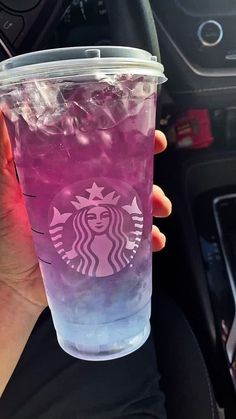 a person holding up a cup with purple liquid on it in their hand and steering wheel behind them