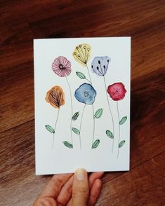 a hand holding up a card with watercolor flowers on it