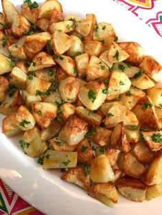 a white plate topped with potatoes and parsley on top of a colorful table cloth