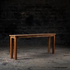 a wooden table sitting on top of a cement floor next to a brick wall with light coming through it