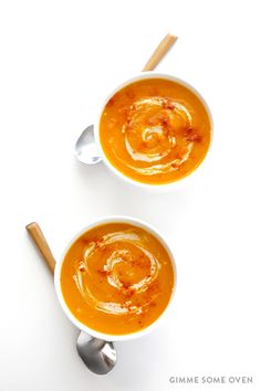 two bowls of carrot soup on a white surface