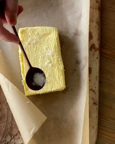 a person scooping sugar from a block of butter on top of parchment paper with a spoon