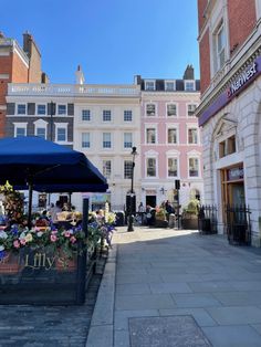 an outdoor cafe with blue umbrella and flowers on the sidewalk in front of some buildings