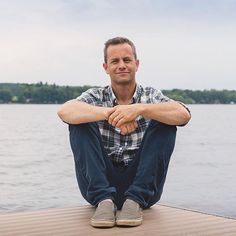 a man sitting on top of a wooden dock next to the water with his arms crossed