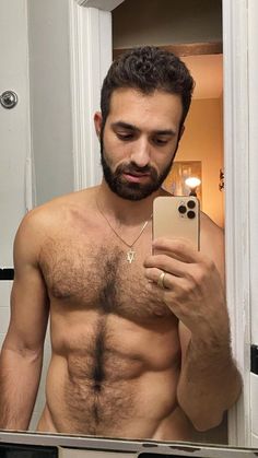 a shirtless man taking a selfie in front of a mirror with his cell phone