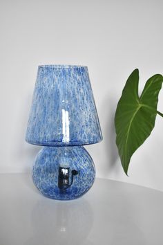 a blue table lamp with a green plant next to it