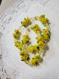 a necklace made out of yellow flowers on a lace doily with green leaves and beads