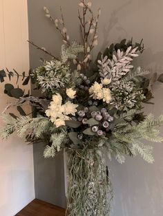 a vase filled with flowers and greenery on top of a hard wood floor next to a wall