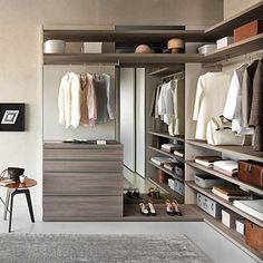 a walk in closet filled with lots of drawers and clothes hanging on the shelves next to a chair