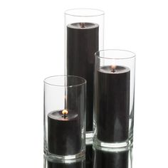 three glass vases with candles in them on a white surface, one is black and the other is clear