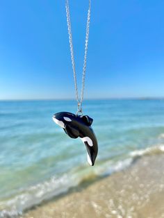 a black and white orca whale necklace hanging from a silver chain on the beach