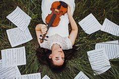 a woman laying on the ground with a violin in her hands and sheet music scattered around her