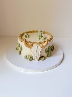 a white cake with green and gold decorations sitting on top of a white platter