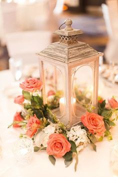 a lantern with flowers and greenery sits on a table in front of other place settings