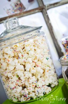 a green table topped with a glass jar filled with popcorn and sprinkles