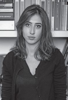 a black and white photo of a woman standing in front of bookshelves with her hands on her hips