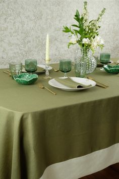 the table is set with green glassware and white flowers in vases on it