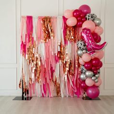 pink, silver and gold balloon arch with cowboy boot balloons on it in front of a white wall