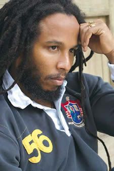 a man with dreadlocks is sitting down and looking off to the side while holding his hand on his head