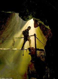 a man walking across a suspension bridge in a cave