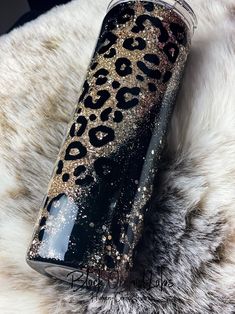 a black and gold leopard print tumbler sitting on top of a white fur rug