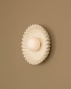 an egg sitting on top of a white plate next to a brown wall in the shape of a shell