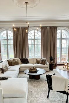 a living room filled with lots of furniture next to large window covered in drapes