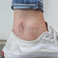 a small tattoo on the ankle of a woman's left foot with a hand holding a flower