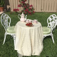 a table with two chairs and a tea pot on it in the grass next to some flowers