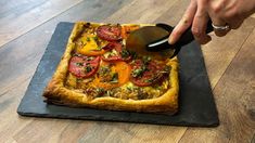 a person cutting into a pizza on top of a black stone slab with a spatula