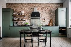 a kitchen with green cabinets and brick wall behind the countertop, along with black chairs