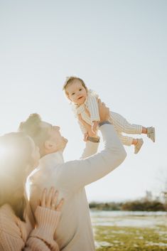 a woman holding a baby up in the air while standing next to a man with his arms around her