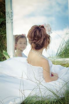 a woman sitting in front of a mirror wearing a white dress and pearls on her head