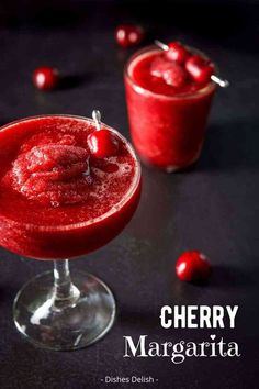 two glasses filled with cherry margaritas on top of a black table next to cherries