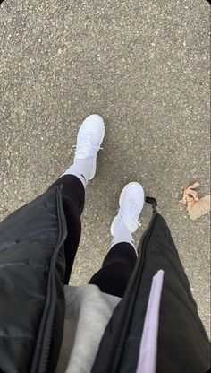 the bottom view of someone's feet wearing white sneakers and black pants, standing on pavement