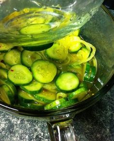 sliced cucumbers in a glass bowl on a counter top, with oil being poured over them