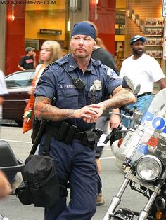 a police officer standing next to his motorcycle in the street with people walking around him