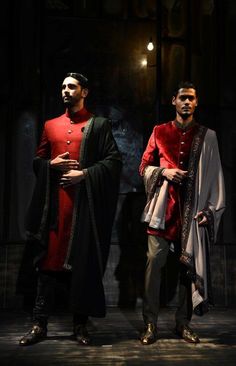 two men standing next to each other wearing red and black outfits with gold accents on them