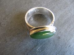 This unique ring is made with an oval BC jade and sterling silver. The jade comes from British Columbia, Canada and is cut in a long oval shape. It is a beautiful deep green. I set the stone horizontally in a fine and sterling silver setting. The band is 7mm wide and textured with powdered silver that I fused to sterling silver. The edges of the band are hammer textured. Ring top measures 14mm by 22mm Ring is size 9 1/4. (The wide band fits size 8 1/2 nicely) Lovely! Modern Oval Green Jewelry, Modern Oval Jade Jewelry, Modern Oval Jade Ring, Modern Green Oval Cabochon Jewelry, Unique Oval Jade Rings, Power Ring, Band Fits, Dendritic Opal, Textured Ring