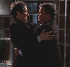 two men hugging each other in the middle of a room with glass doors and windows