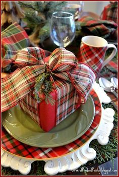 a christmas table setting with red and green plaid napkins, wrapped present box on plate