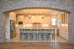 an open kitchen and dining room area with brick walls, white cabinets and wood flooring