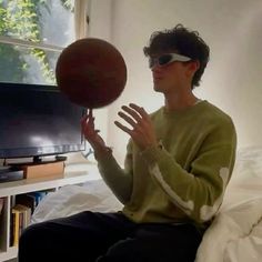 a person sitting on a bed with a basketball in their hand and a tv behind them