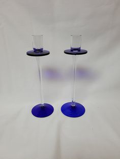 two blue glass candlesticks sitting side by side on a white background, with one candle in the middle