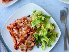 a white plate topped with lasagna next to a salad on top of a blue table