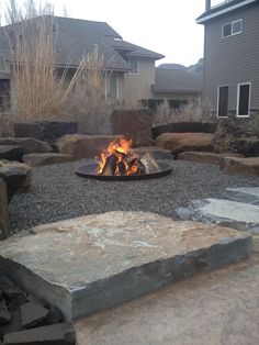 a fire pit in the middle of a yard with rocks around it and grass on either side