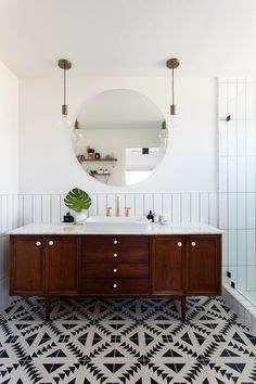 a bathroom with black and white tile flooring and a round mirror on the wall